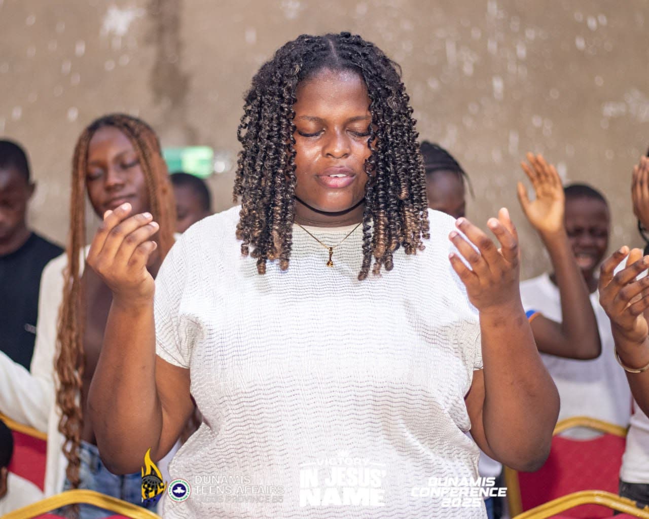 A teenager worshipping with her hands raised and eyes closed